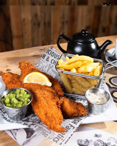 crispy fish and golden fries with mushy peas and sauce and lemon in a plate with a tea pot served at The Village Fish Bar Neilston